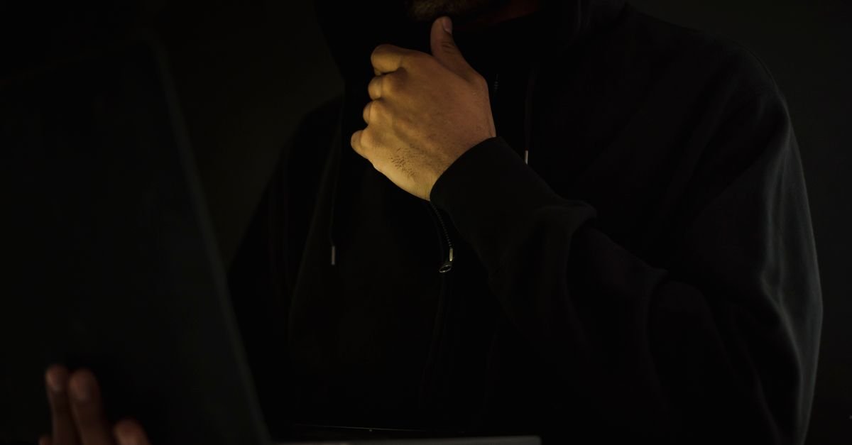 Homem de capuz usa notebook no escuro, imagem que ilustra fraude eletrônica