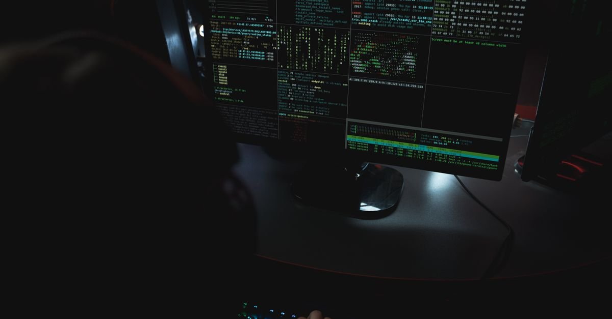Telas de computador com código em sala escura, em referência a invasão de sistema