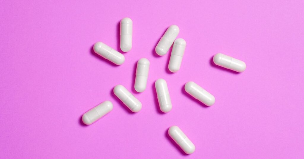 Cápsulas brancas de medicamento espalhadas sobre superfície colorida