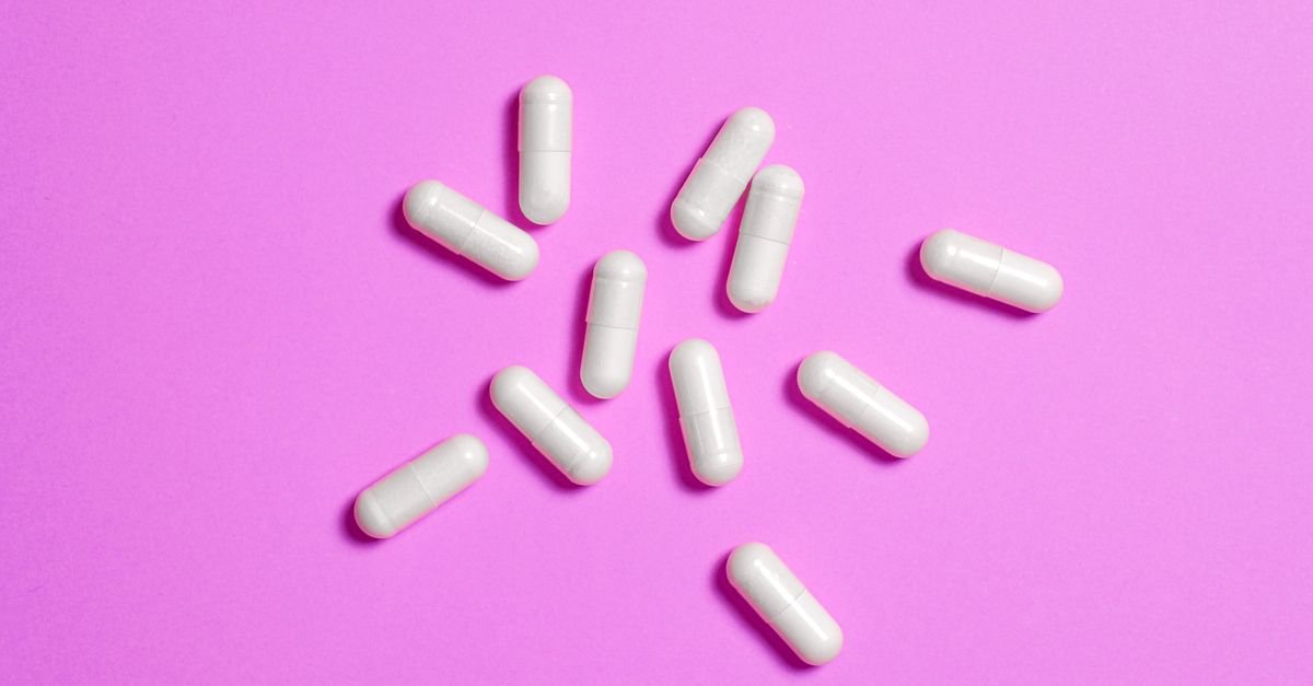 Cápsulas brancas de medicamento espalhadas sobre superfície colorida
