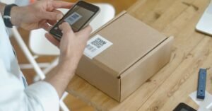 Pessoa usa celular para ler codigo QR em caixa de encomenda sobre mesa de madeira