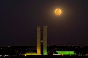 Fachada do Congresso Nacional iluminada à noite, com a lua ao fundo