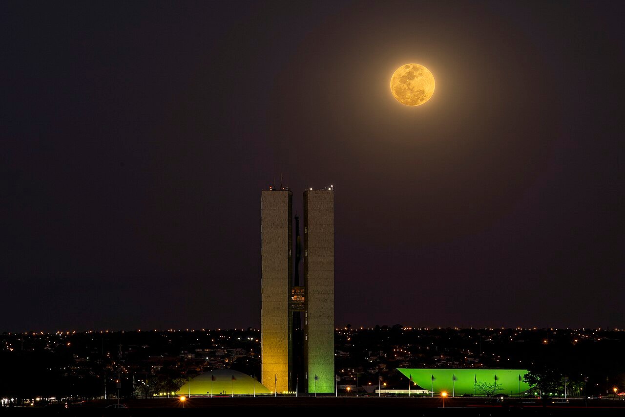 Fachada do Congresso Nacional iluminada à noite, com a lua ao fundo