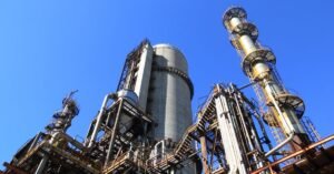 Torres e tubulações de uma unidade de refino de petróleo vistas de baixo sob céu azul