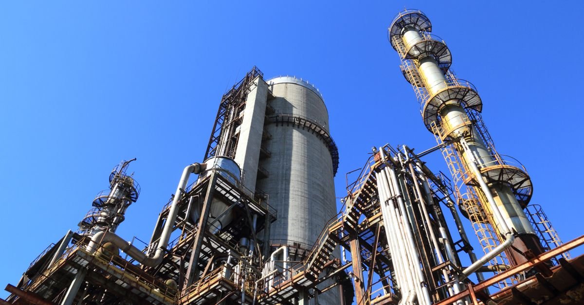 Torres e tubulações de uma unidade de refino de petróleo vistas de baixo sob céu azul