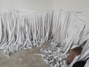 Boletins de urna impressos afixados em parede e separados por zona eleitoral após apuração