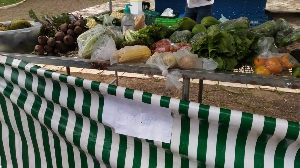 Placa escrita a mao com a palavra Pix presa na lona de uma barraca de feira com verduras e frutas