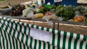 Placa escrita a mao com a palavra Pix presa na lona de uma barraca de feira com verduras e frutas