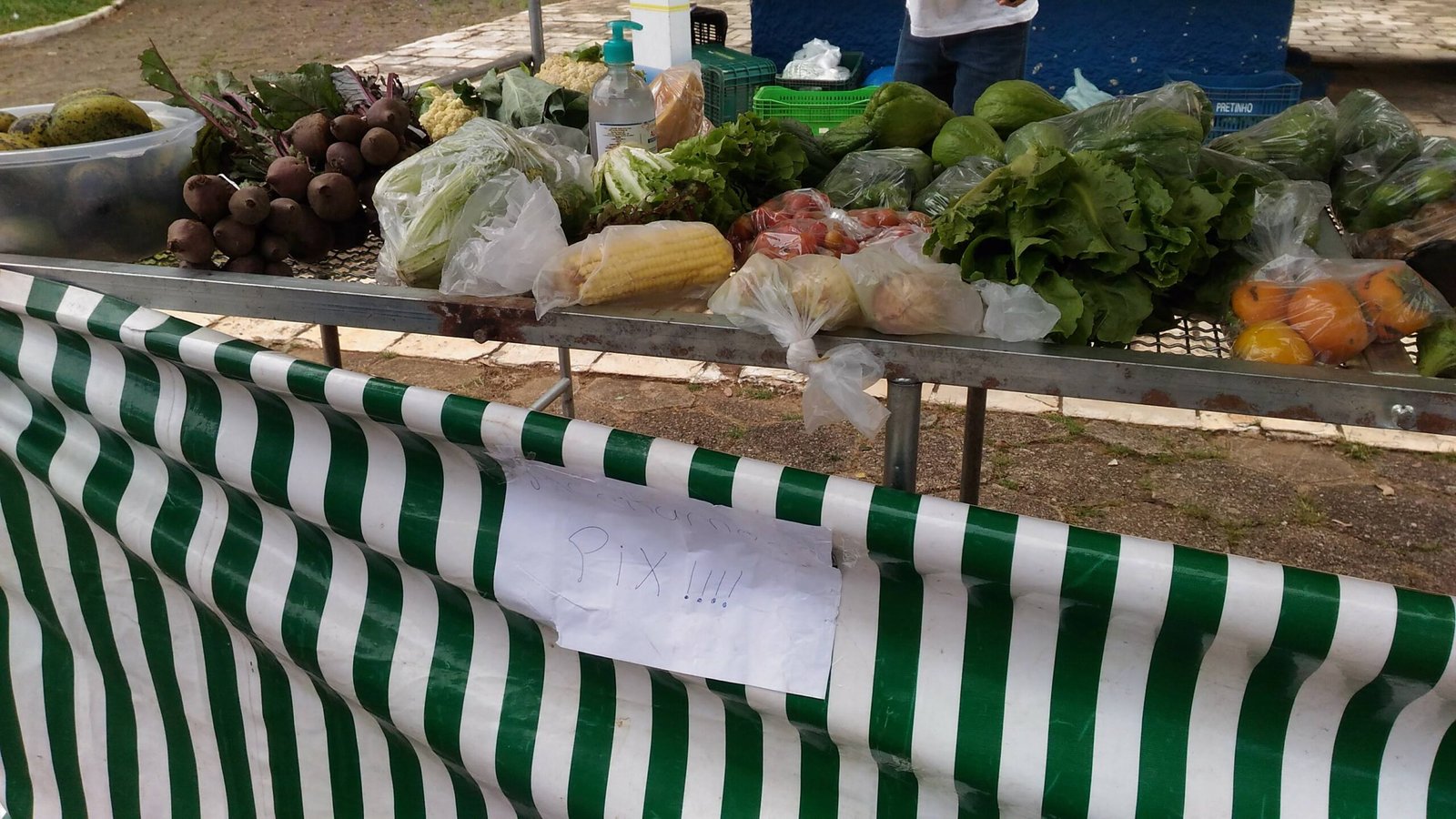 Placa escrita a mao com a palavra Pix presa na lona de uma barraca de feira com verduras e frutas