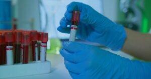 Mãos com luvas azuis segurando tubos de coleta de sangue em laboratório