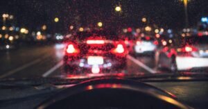 Trânsito noturno visto pelo para-brisa molhado de um carro