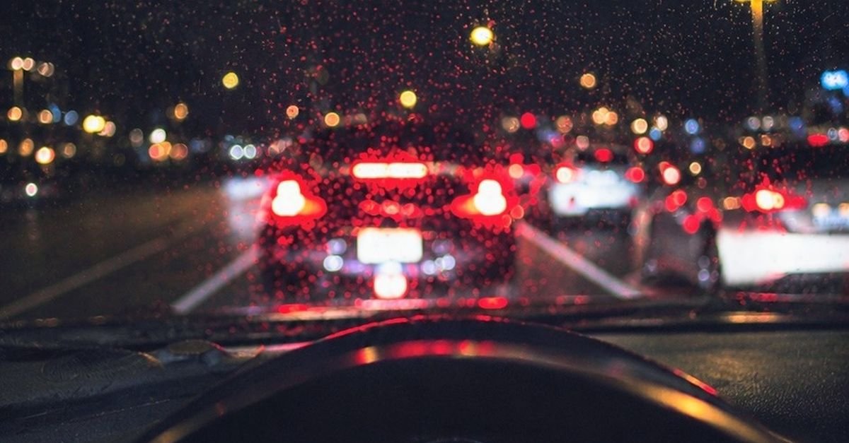 Trânsito noturno visto pelo para-brisa molhado de um carro