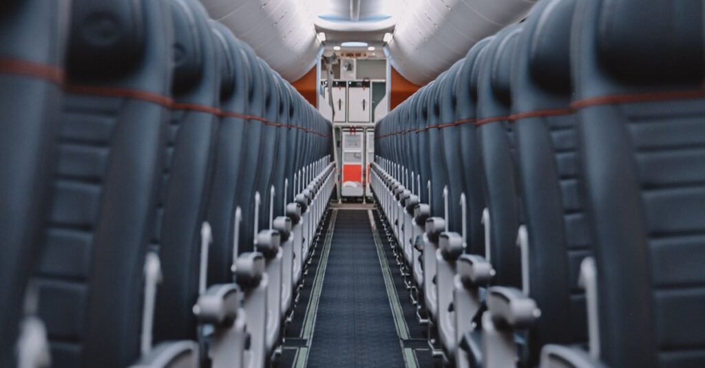 Corredor central de uma cabine de avião comercial vazia, com fileiras de poltronas dos dois lados