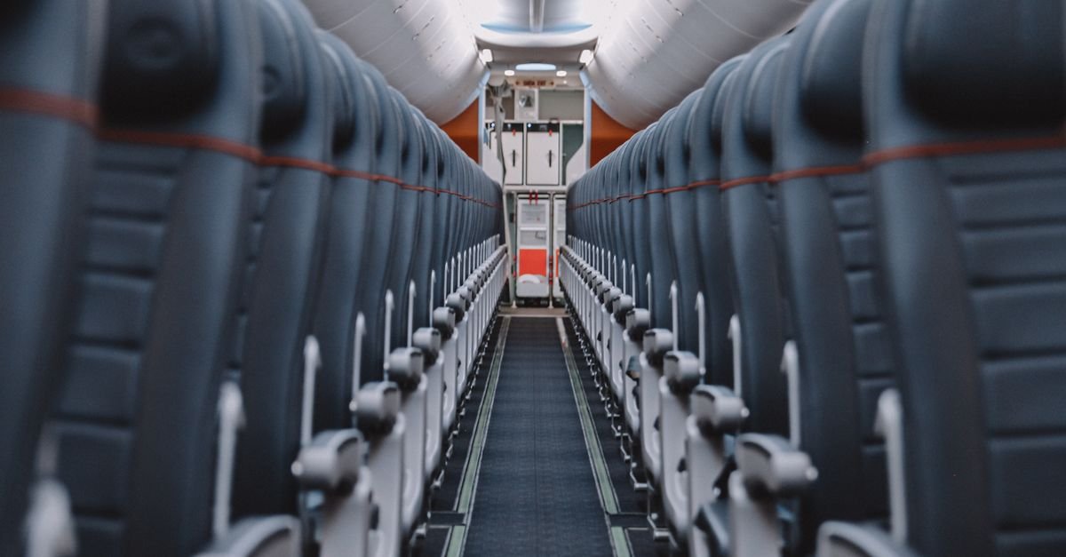 Corredor central de uma cabine de avião comercial vazia, com fileiras de poltronas dos dois lados
