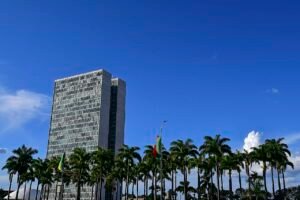 Fachada do edifício do Congresso Nacional em Brasília, com palmeiras em primeiro plano e céu azul