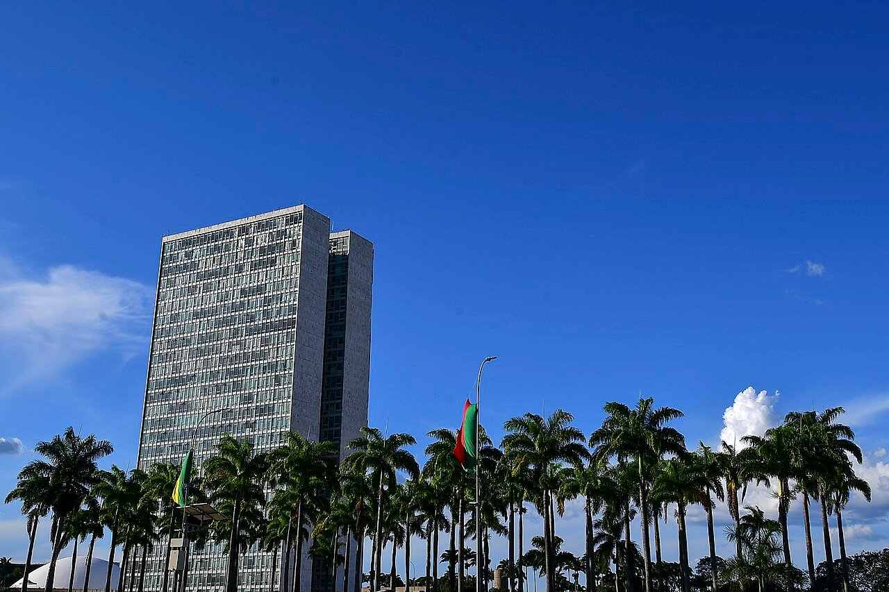 Fachada do edifício do Congresso Nacional em Brasília, com palmeiras em primeiro plano e céu azul
