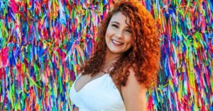 Mulher sorri diante de parede coberta por fitas coloridas
