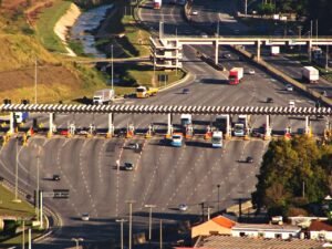 Vista aérea de praça de pedágio em rodovia federal brasileira, com veículos passando pelas cabines
