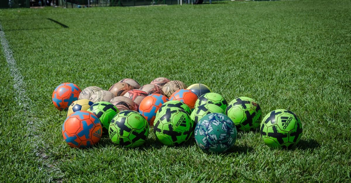 Bolas de futebol reunidas sobre a grama de um campo, ao lado da linha lateral
