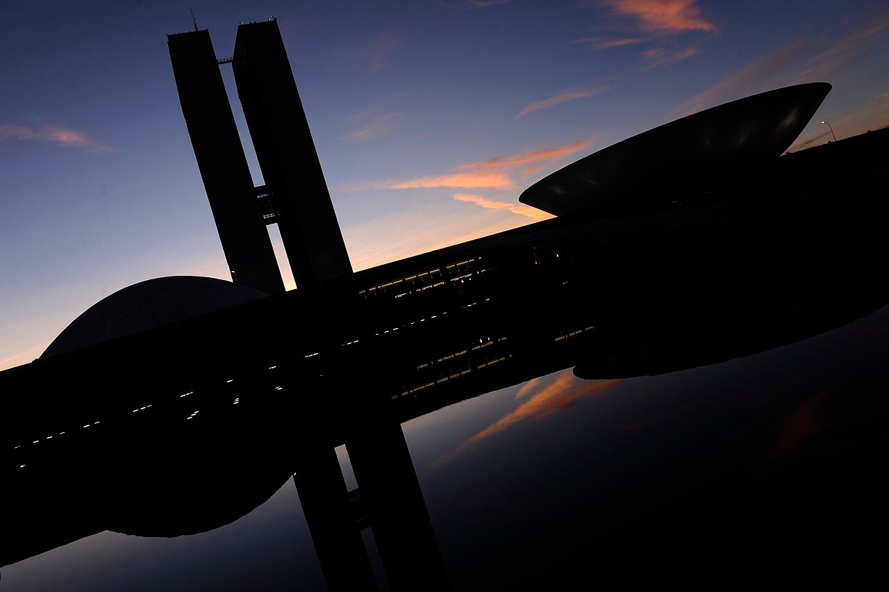 Silhueta do Congresso Nacional ao anoitecer, com as duas torres e as cúpulas refletidas no espelho d'água