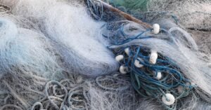 Redes de pesca artesanal empilhadas em close, com boias brancas e cordas azuis