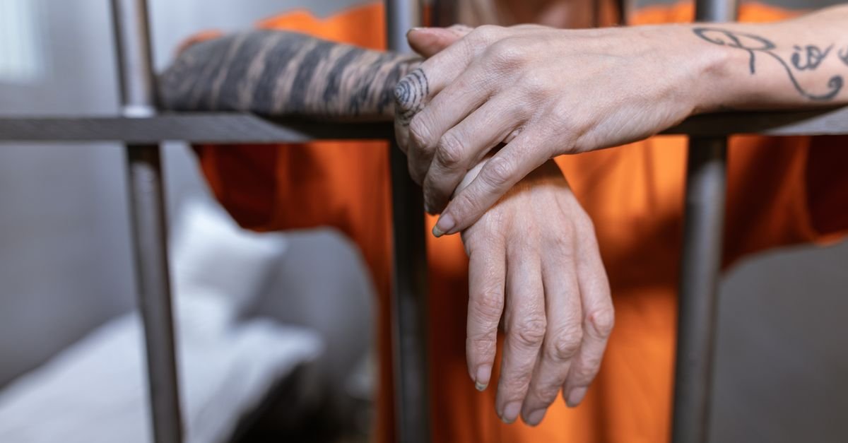 Maos de um detento apoiadas nas grades de uma cela