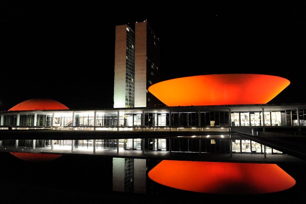 Fachada do Congresso Nacional em Brasília iluminada à noite, com reflexo no espelho d'água