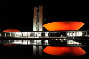 Fachada do Congresso Nacional em Brasília iluminada à noite, com reflexo no espelho d'água