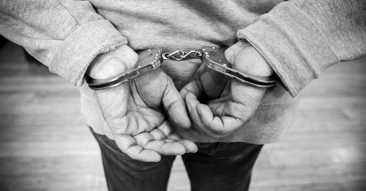 Mãos de pessoa algemadas atrás das costas em imagem em preto e branco