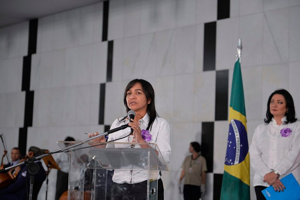Autoridade discursa em púlpito no lançamento da campanha Agosto Lilás, com a bandeira do Brasil ao lado