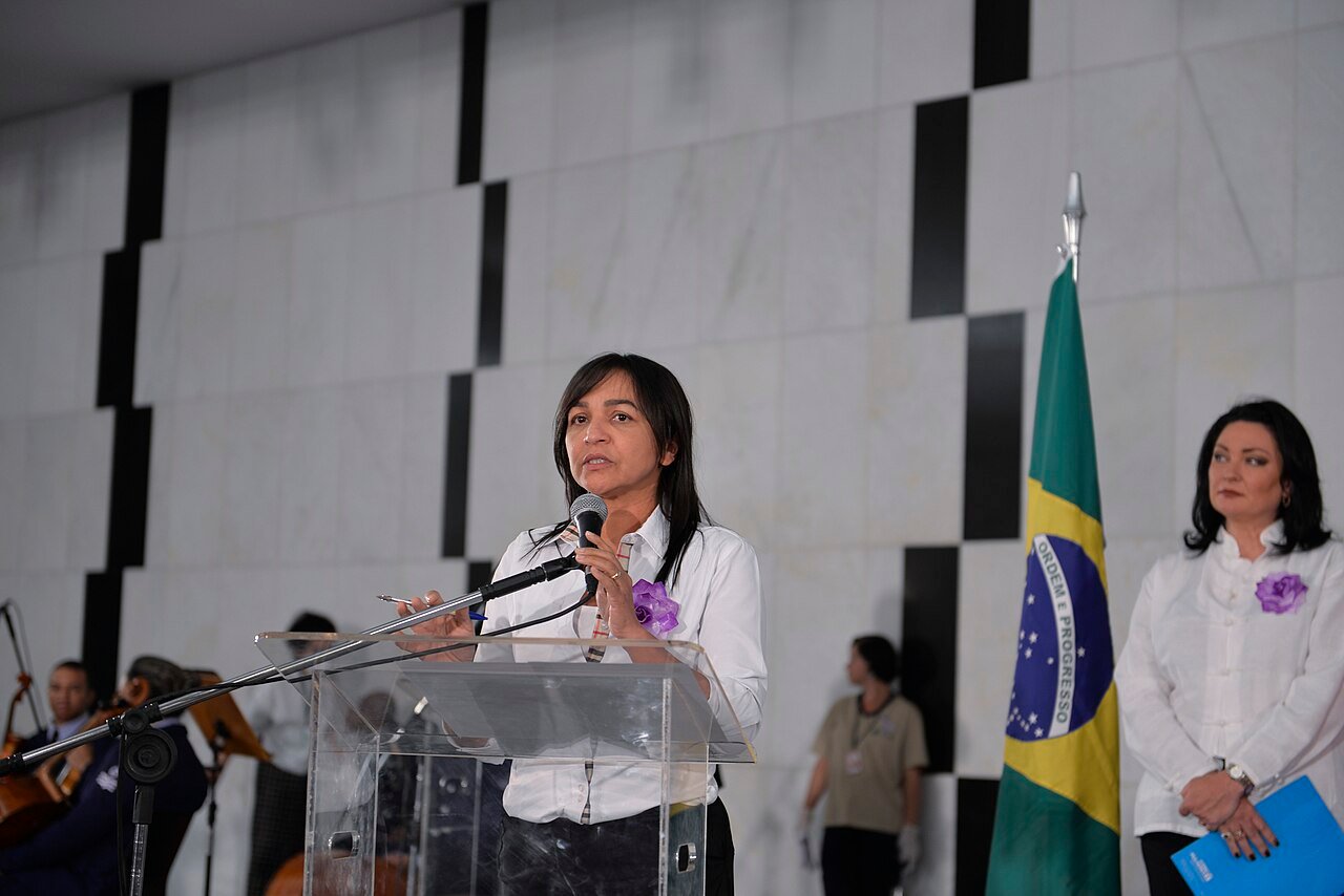 Autoridade discursa em púlpito no lançamento da campanha Agosto Lilás, com a bandeira do Brasil ao lado