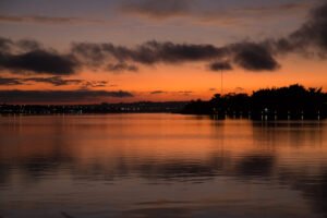 Amanhecer no Lago Paranoá, em Brasília, com a água calma e as luzes da orla ao fundo