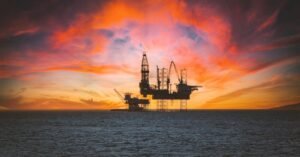 Silhueta de plataforma de petroleo em alto-mar contra ceu alaranjado no fim da tarde