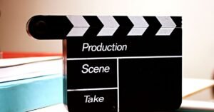 Claquete de cinema preta com campos para produção, cena e take, apoiada sobre uma mesa