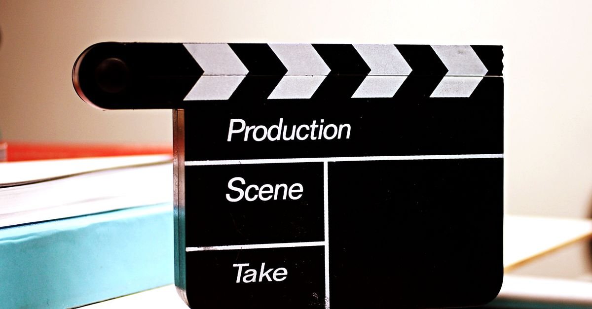 Claquete de cinema preta com campos para produção, cena e take, apoiada sobre uma mesa