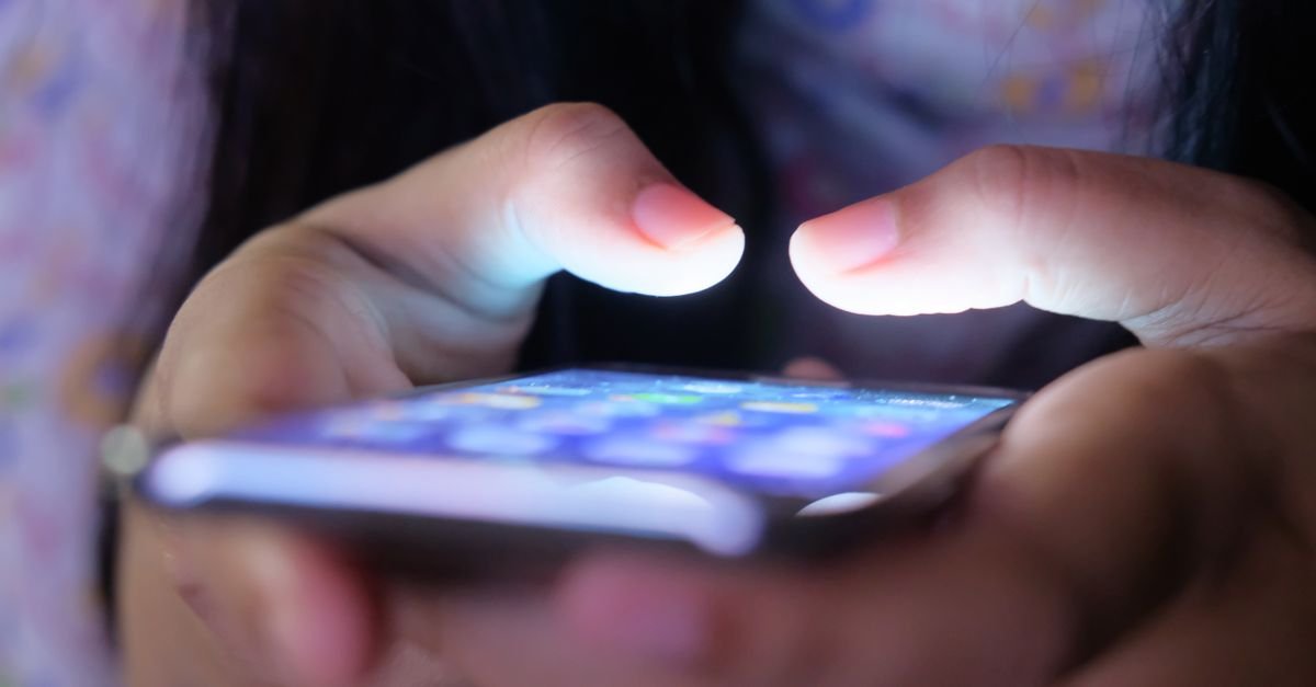 Mãos segurando um celular com a tela acesa no escuro