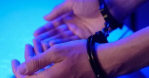 Mãos algemadas em close, sob luz azul de viatura