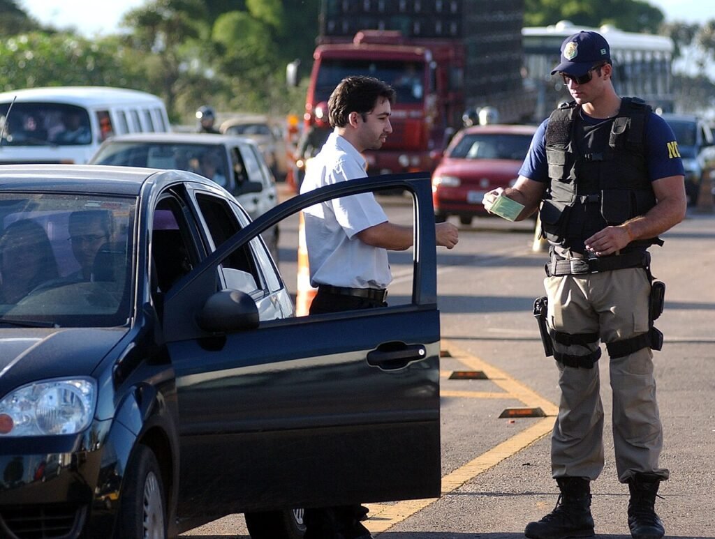 Agente da Policia Rodoviaria Federal fiscaliza motorista parado no acostamento de rodovia federal