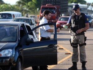 Agente da Policia Rodoviaria Federal fiscaliza motorista parado no acostamento de rodovia federal