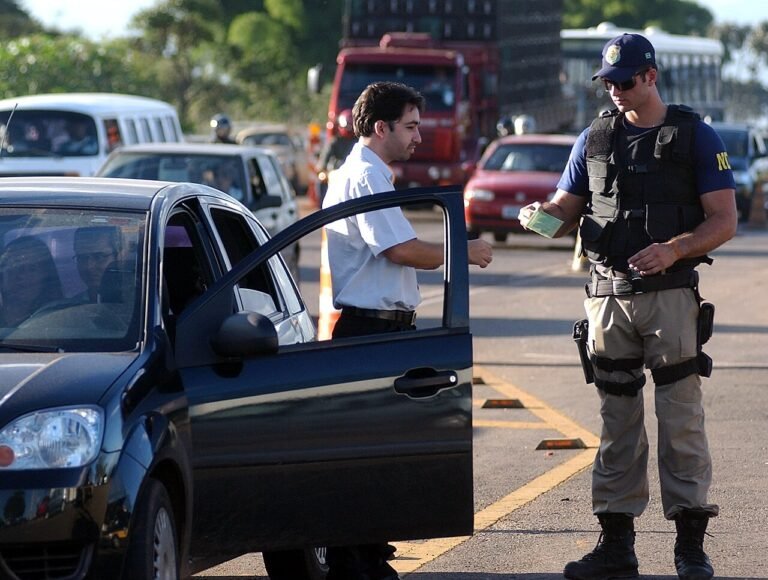Agente da Policia Rodoviaria Federal fiscaliza motorista parado no acostamento de rodovia federal