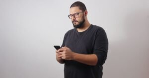 Homem de camiseta escura usa smartphone com as duas mãos