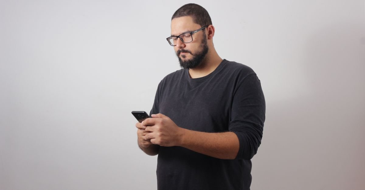 Homem de camiseta escura usa smartphone com as duas mãos