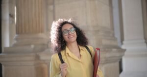 Estudante sorridente com pasta de documentos sob o braço em frente a colunas de prédio