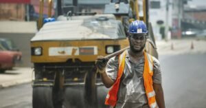 Trabalhador com capacete e colete de segurança em obra de pavimentação de rua no Brasil