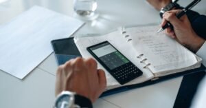 Pessoa usa calculadora e anota cálculos em caderno sobre mesa de escritório