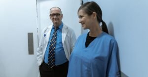 Medico de jaleco branco e enfermeira de uniforme azul conversam em corredor de hospital