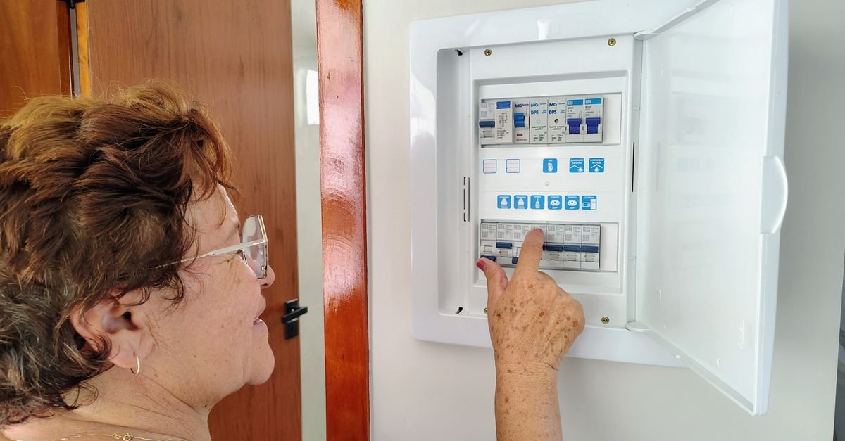 Mulher aciona disjuntor em quadro de energia residencial