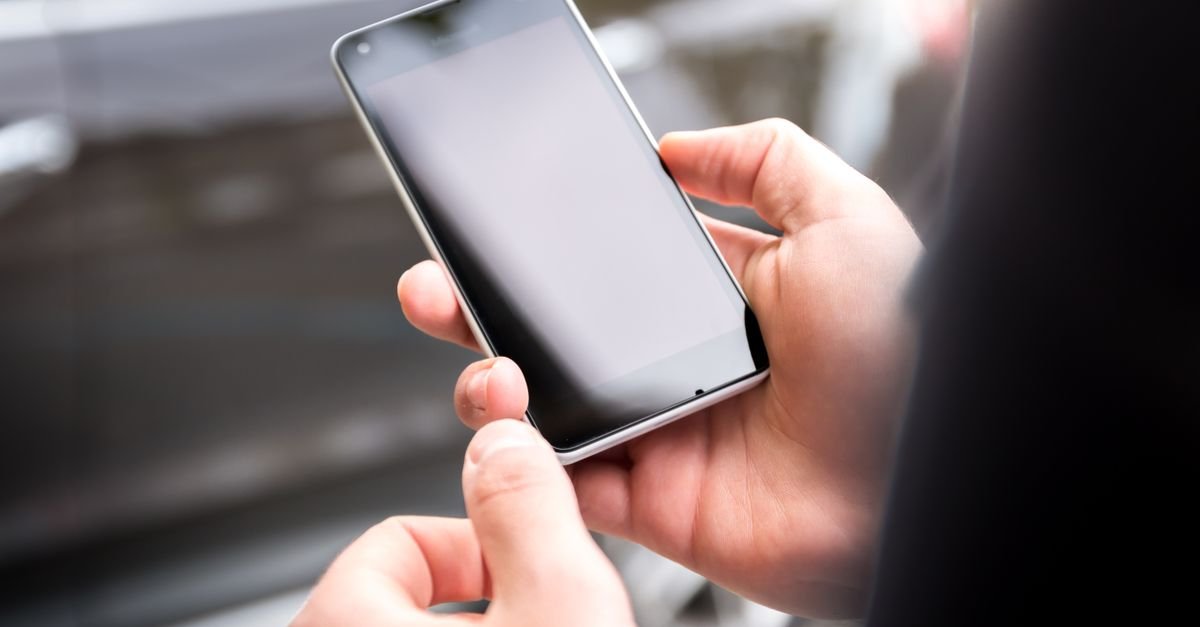 Mãos segurando um celular com a tela apagada, ilustrando a consulta à restituição pelo aplicativo