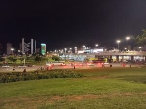 Rodoviária do Plano Piloto vista à noite, com ônibus na plataforma, viaduto iluminado e prédios de Brasília ao fundo