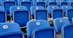 Fileiras de cadeiras azuis numeradas em arquibancada vazia de estádio